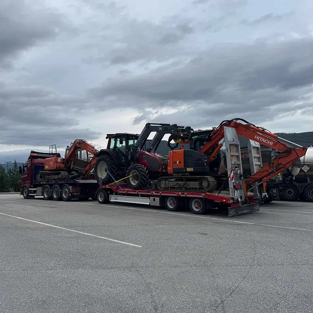 Tungtransport med traktor og flere gravemaskiner på spesialhenger, parkert ved veiskulder.