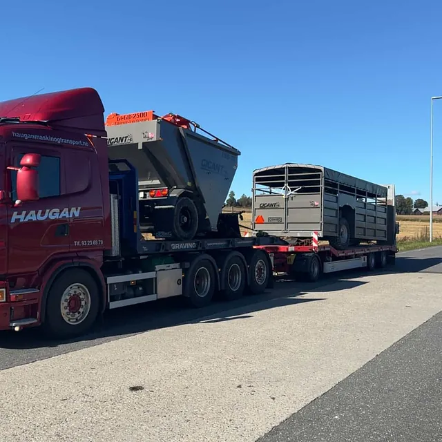 Rød Haugan-lastebil parkert på veiskulder ved Nordby, frakter landbruksvogner fra Gigant.